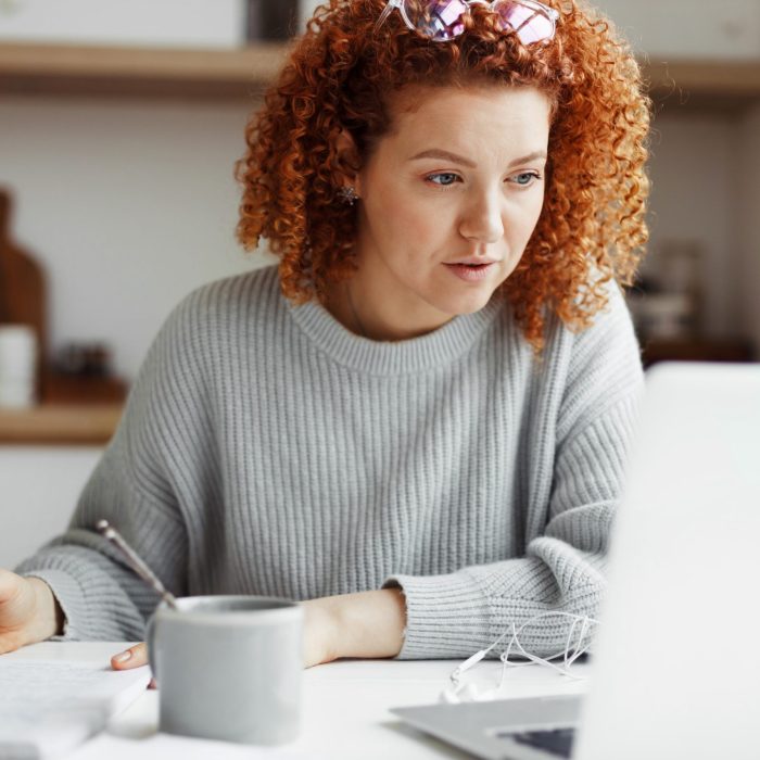 Portrait of attractive redhead caucasian businesswoman in casual clothes working from home, making business plan for launching new project, checking e-mail and financial report from her accountant